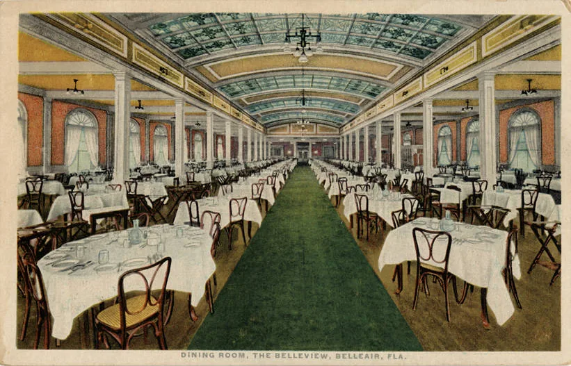 The grand hotel dining hall: rows of white-clothed tables down a long green-carpeted room under a stained-glass skylight ceiling.