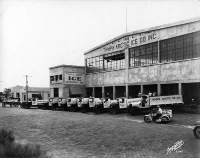 About ten early ice-delivery trucks lined up in a row in front of a building painted 'Tampa Arctic Ice Co. Inc.'