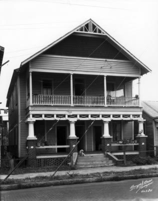 A two-story wood-frame house with a full-width columned porch on both floors; laundry hangs on the upper porch and a dog sits on the front steps.