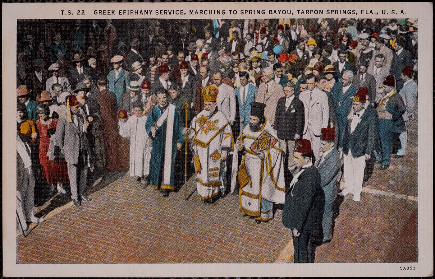 A hand-colored period postcard of a dense crowd on a brick street, with an Orthodox archbishop in gold vestments and mitre, priests, and men wearing red fezzes processing through the middle.